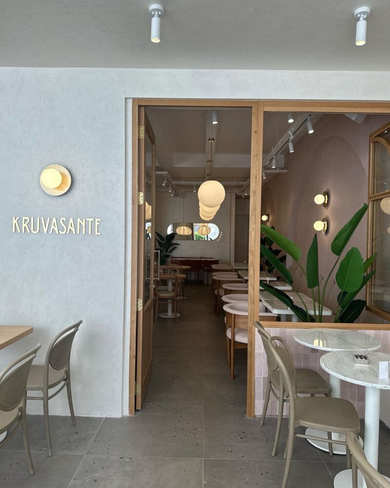 Vue sous un autre angle du café-restaurant décoré tout en rose, avec des tables en marbre ou terrazzo à pieds blancs et des chaises assorties