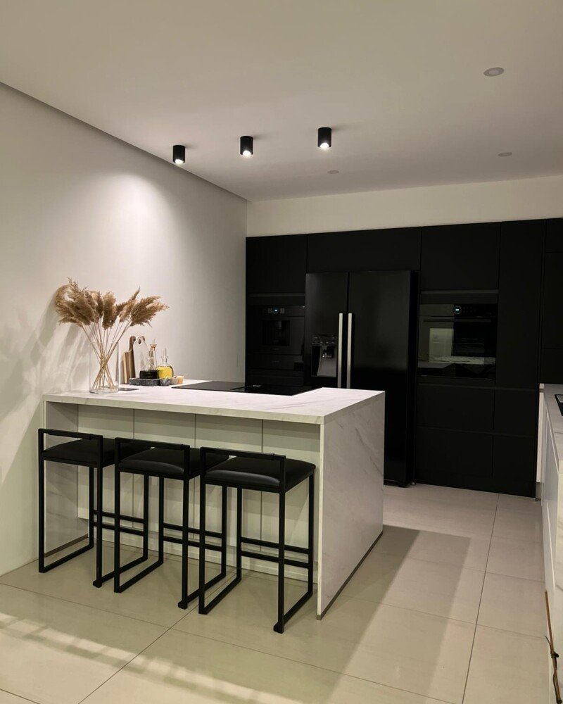 Cuisine moderne avec plan de travail en marbre blanc veiné de gris, chaises de bar en métal et ambiance épurée